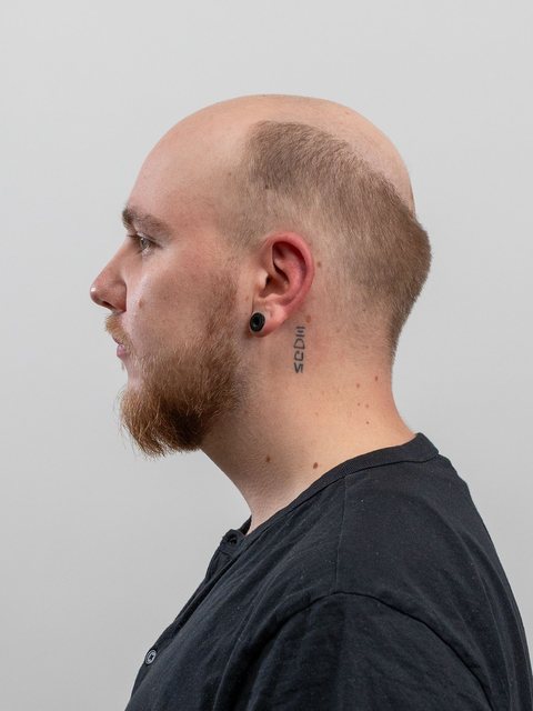 A man photographed from the side against a plain wall